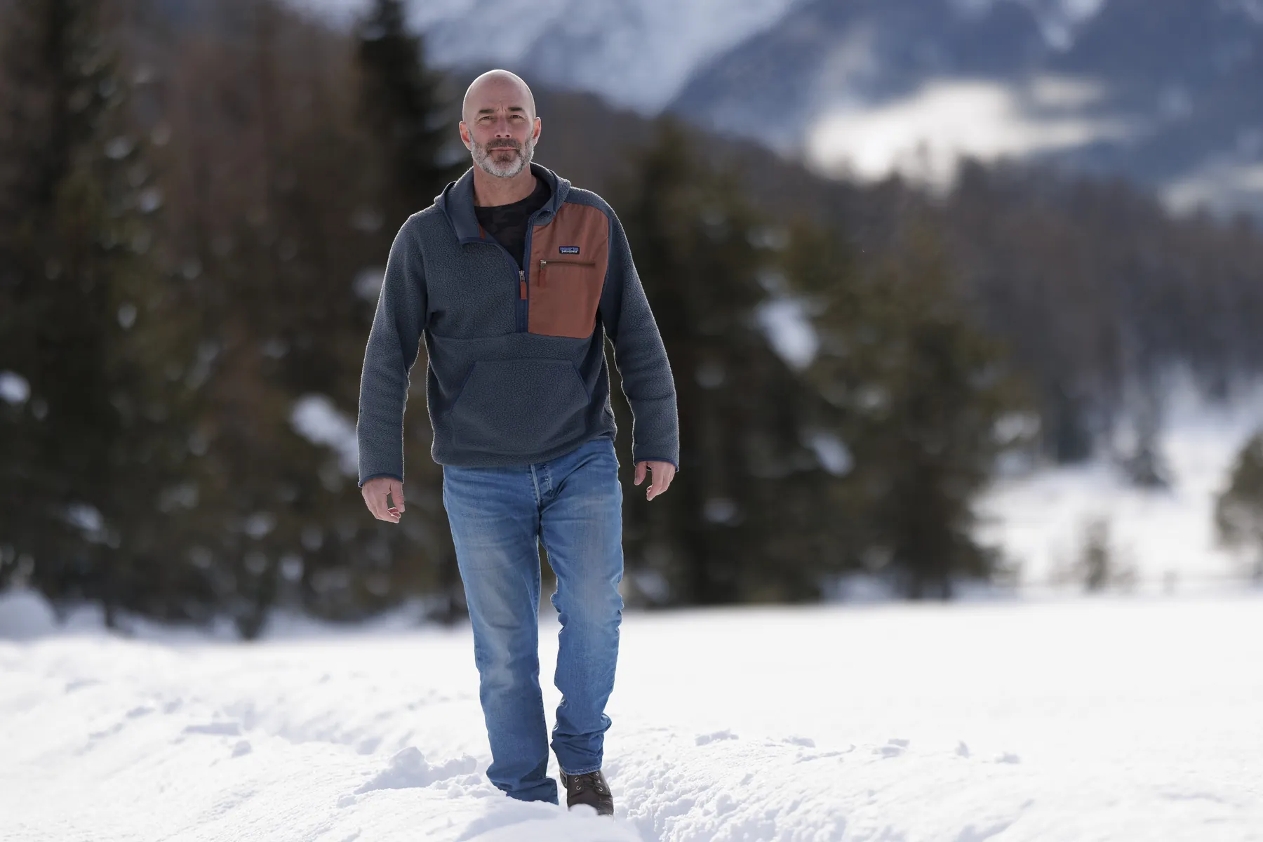 Cla Mosca geht im Engadin durch tiefen Schnee auf die Kamera zu, Lärchen und Berge im Hintergrund.